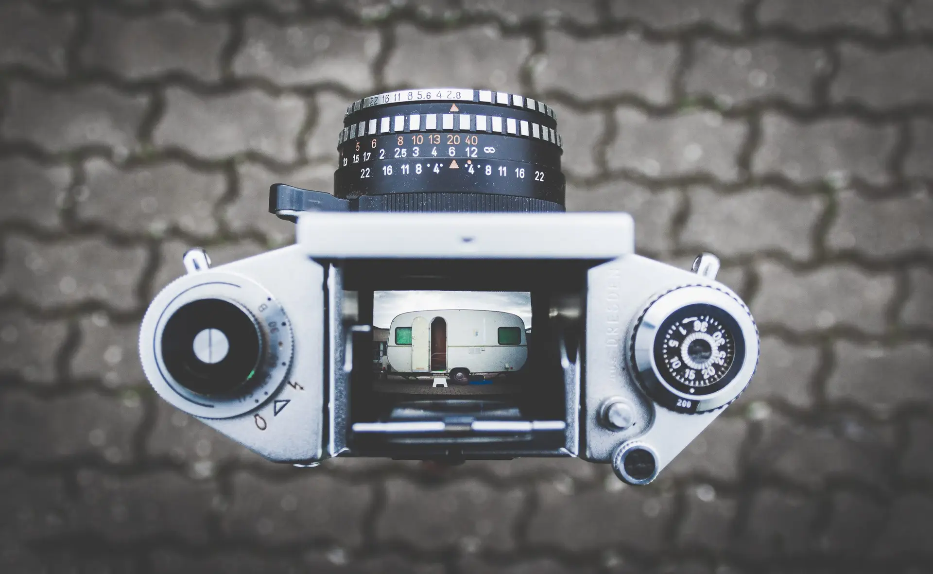 Eine Vintage-Kamera zeigt den Blick durch den Sucher auf einen Wohnwagen, der scharf fokussiert ist, während der Hintergrund unscharf bleibt. Das Bild symbolisiert Präzision und den kreativen Prozess in der Werbefilmproduktion.