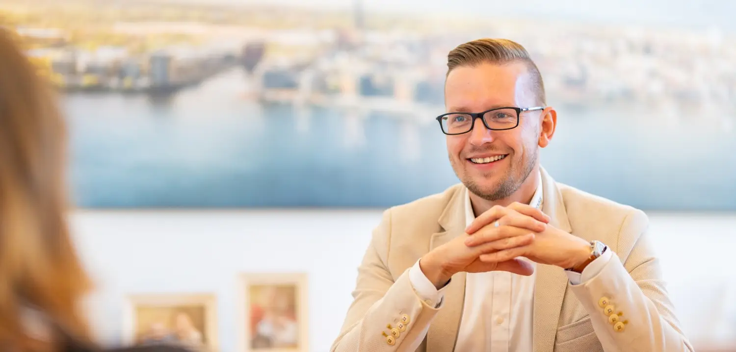 Ein lächelnder Mitarbeiter in einem Recruiting-Gespräch bei Mare Finanz in Rostock, im Hintergrund ein unscharfes Bild der Skyline am Wasser. Das Foto vermittelt Professionalität und Offenheit.