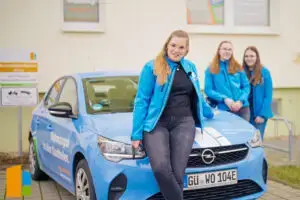 Die Azubis der WGG und Svea aus der Abteilung Technik stehen am blauen Dienstwagen mit Beschriftung der WGG. Das Foto entstand beim Dreh des Azubi-Filmes der WGG im Februar 2024.