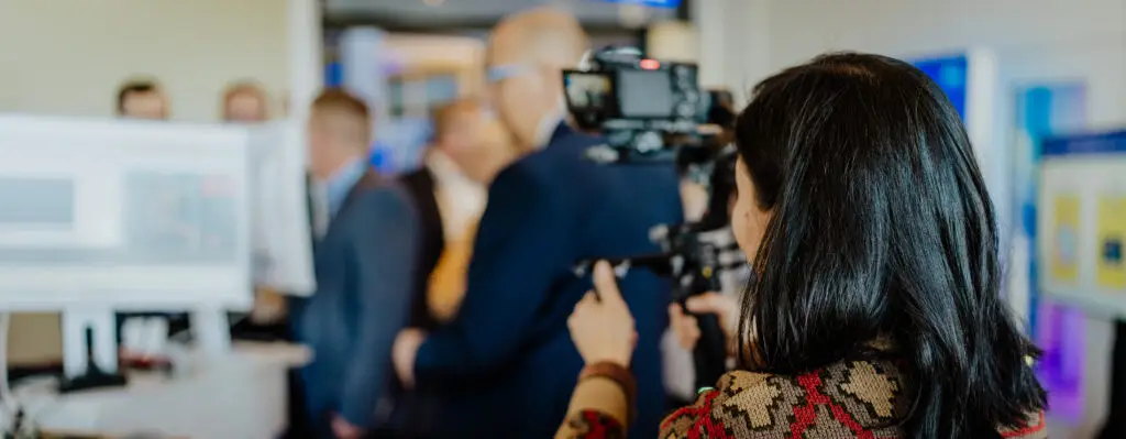 Videografin filmt eine Business-Veranstaltung mit mehreren Personen in einem Messeumfeld.