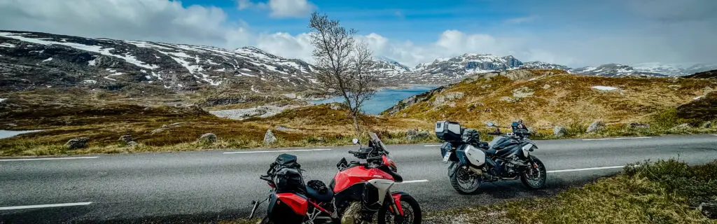 Motorradreise Norwegen – zwei Motorräder auf einer Panoramastraße mit Blick auf schneebedeckte Berge und Fjord