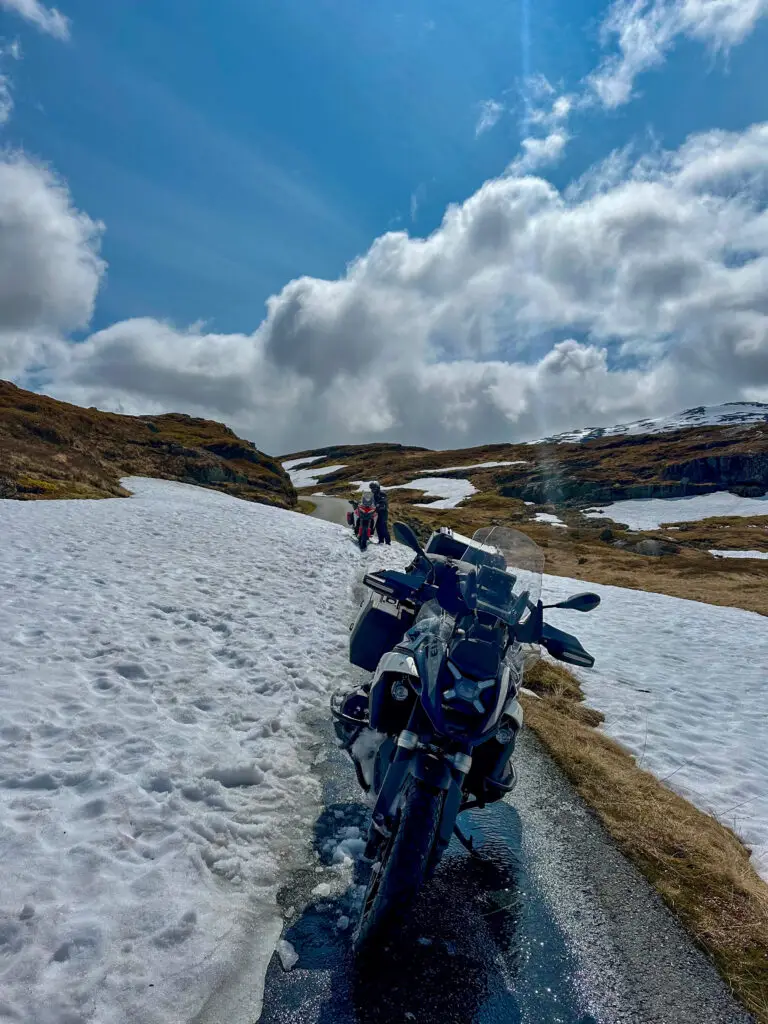 Motorradreise Norwegen – Motorrad auf Bergstraße zwischen Schneefeldern unter blauem Himmel