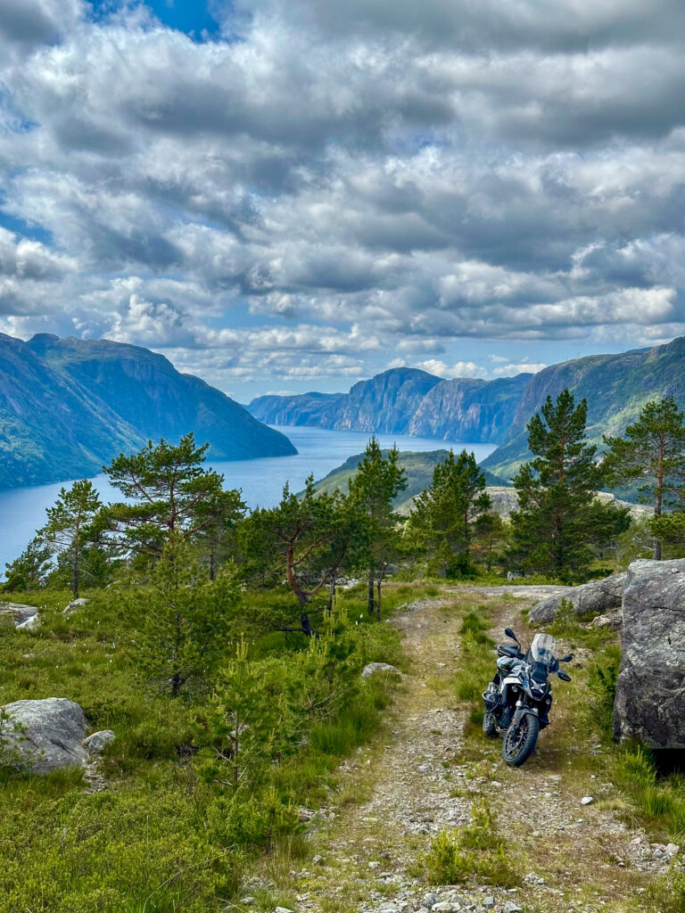 Motorradreise Norwegen – Motorrad auf Bergpfad mit Blick auf einen tief eingeschnittenen Fjord und steile Felswände