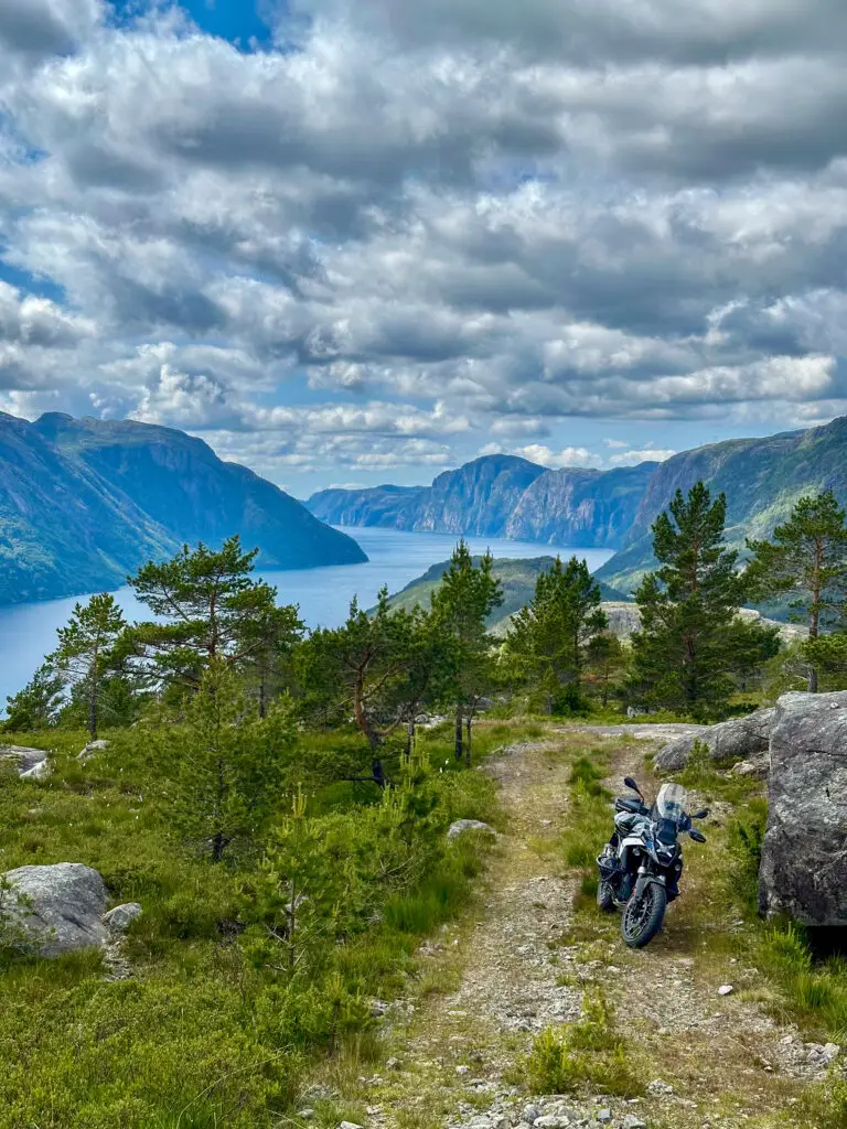 Motorradreise Norwegen – Motorrad auf Bergpfad mit Blick auf einen tief eingeschnittenen Fjord und steile Felswände