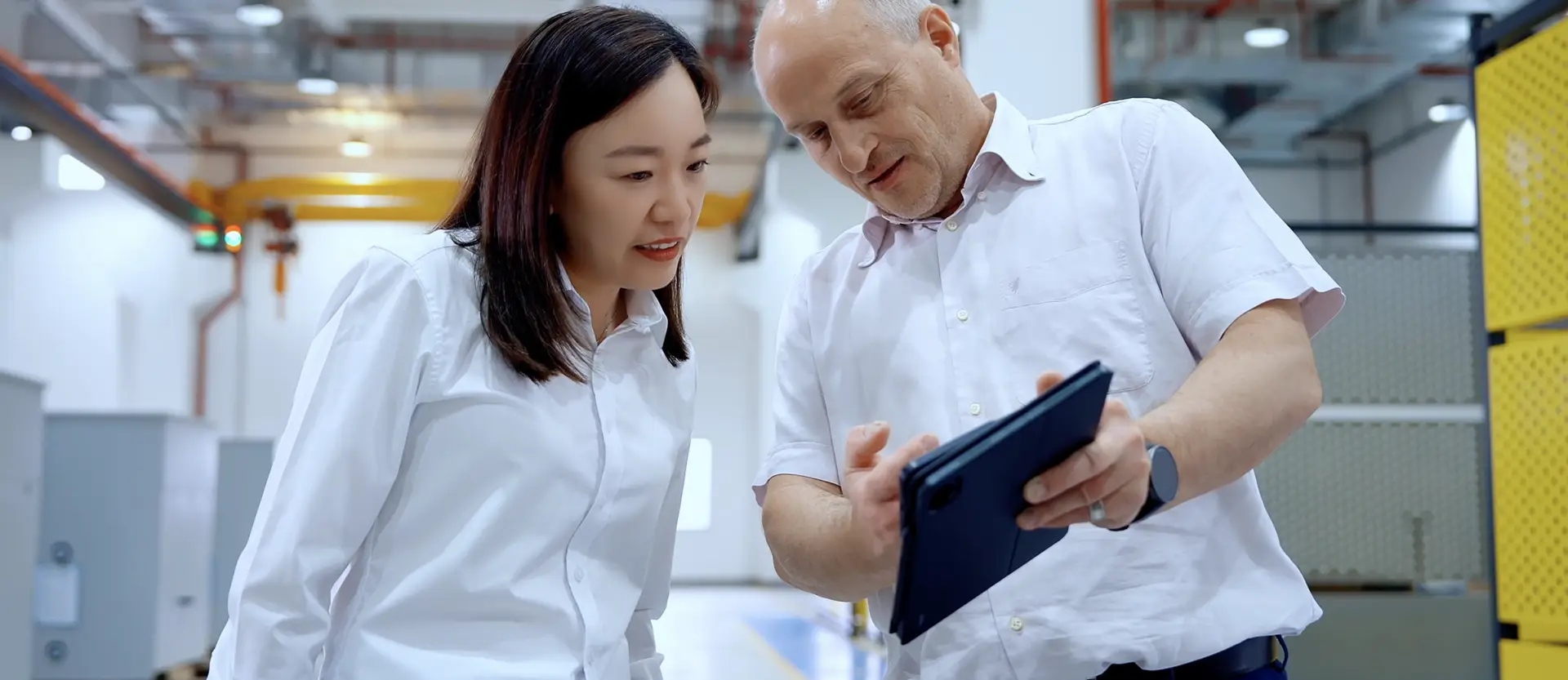 Zwei Fachkräfte in einer Industriehalle betrachten ein Tablet zur Planung von Video Marketing für Unternehmen