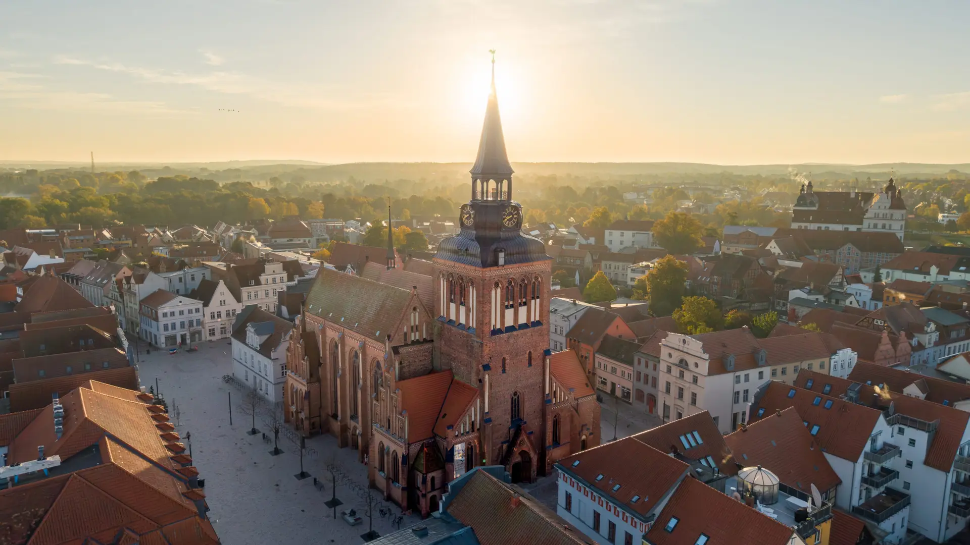 Drohnenaufnahme der Marienkirche in Güstrow bei tief stehender Sonne mit Blick über die historische Altstadt und das Güstrower Schloss