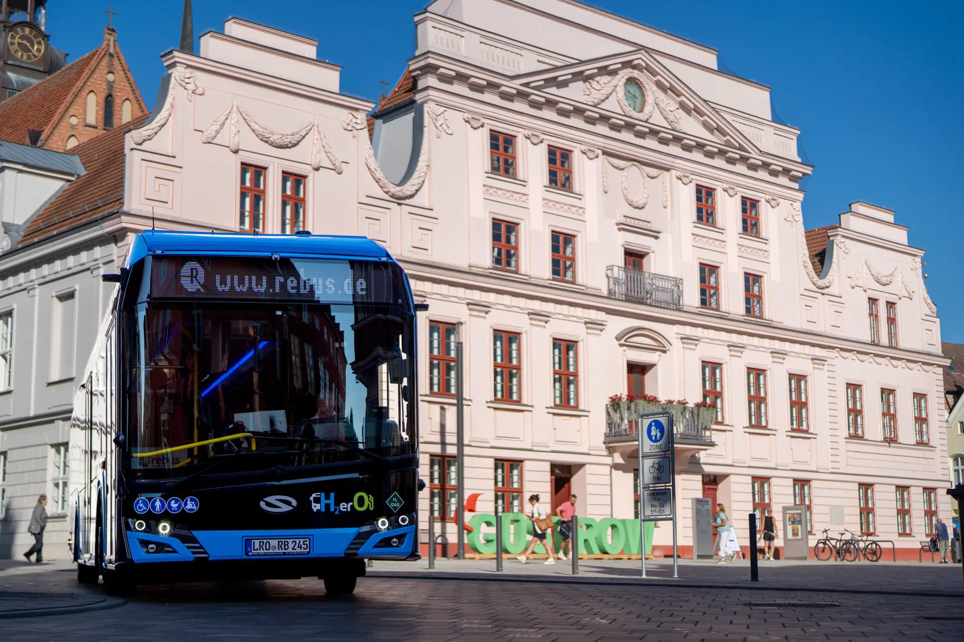 Blau-schwarzer Wasserstoffbus von rebus Regionalbus Rostock vor dem historischen Rathaus in Güstrow, fotografiert für die Unternehmensfotografie.